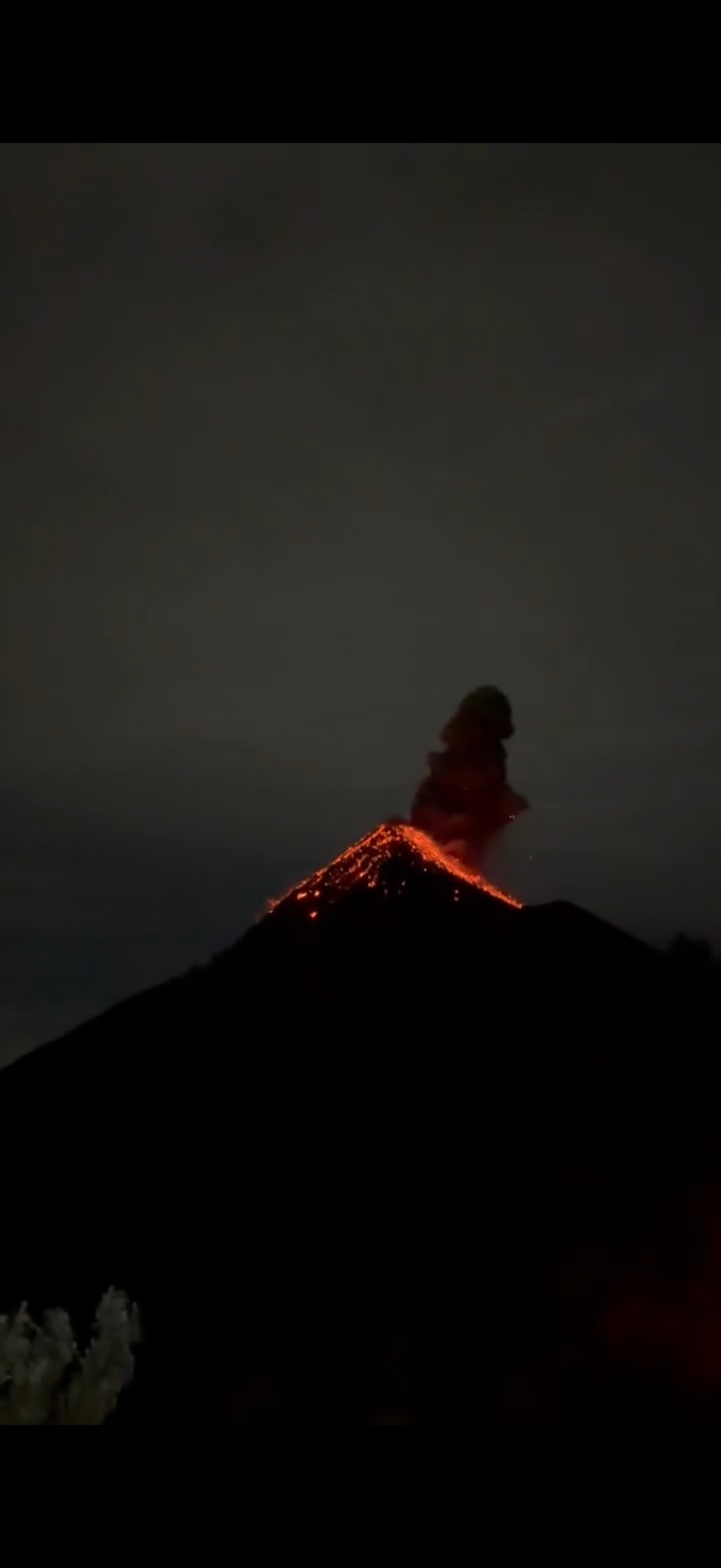 Glowing lava spilling down a volcano in Guatemala during a nighttime eruption, with a plume above the summit.